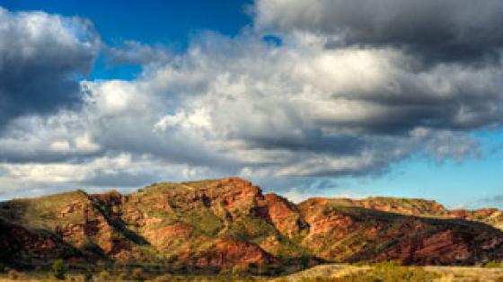 Red-hued cliffs under a blue sky with puffy clouds