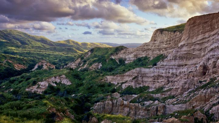 Large colorful cliff with green valley below and puffy clouds above