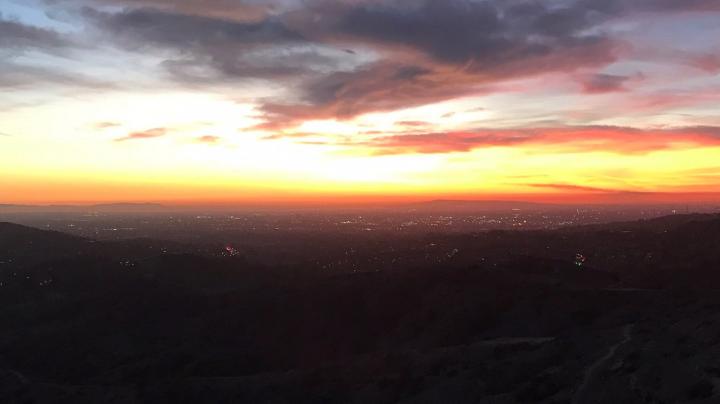 Cloudy orange and yellow sky at sunset over a dark cityscape view