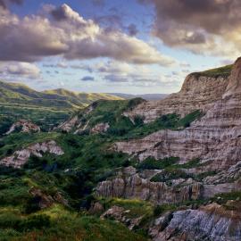 Large colorful cliff with green valley below and puffy clouds above