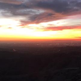 Cloudy orange and yellow sky at sunset over a dark cityscape view