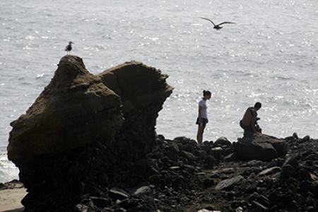 Two people stand on a rocky outcropping overlooking the ocean